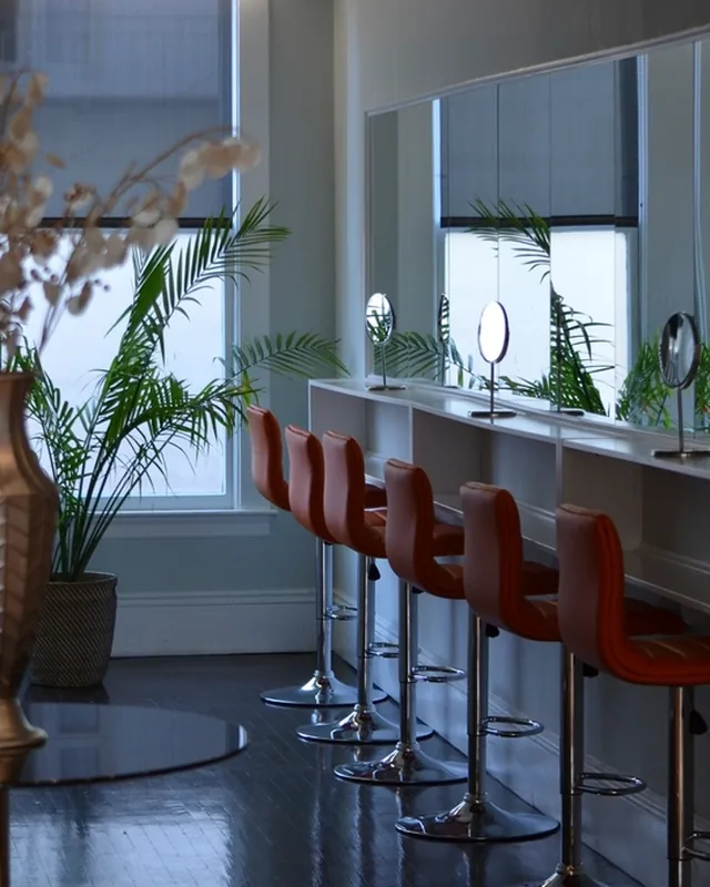 Salon de coiffure avec fauteuils rouges alignés devant les miroirs.